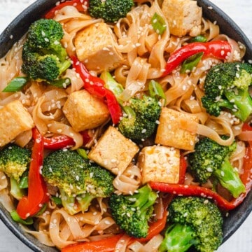 Sweet & sour tofu, broccoli, noodles, and red bell pepper topped with sesame seeds in a bowl.