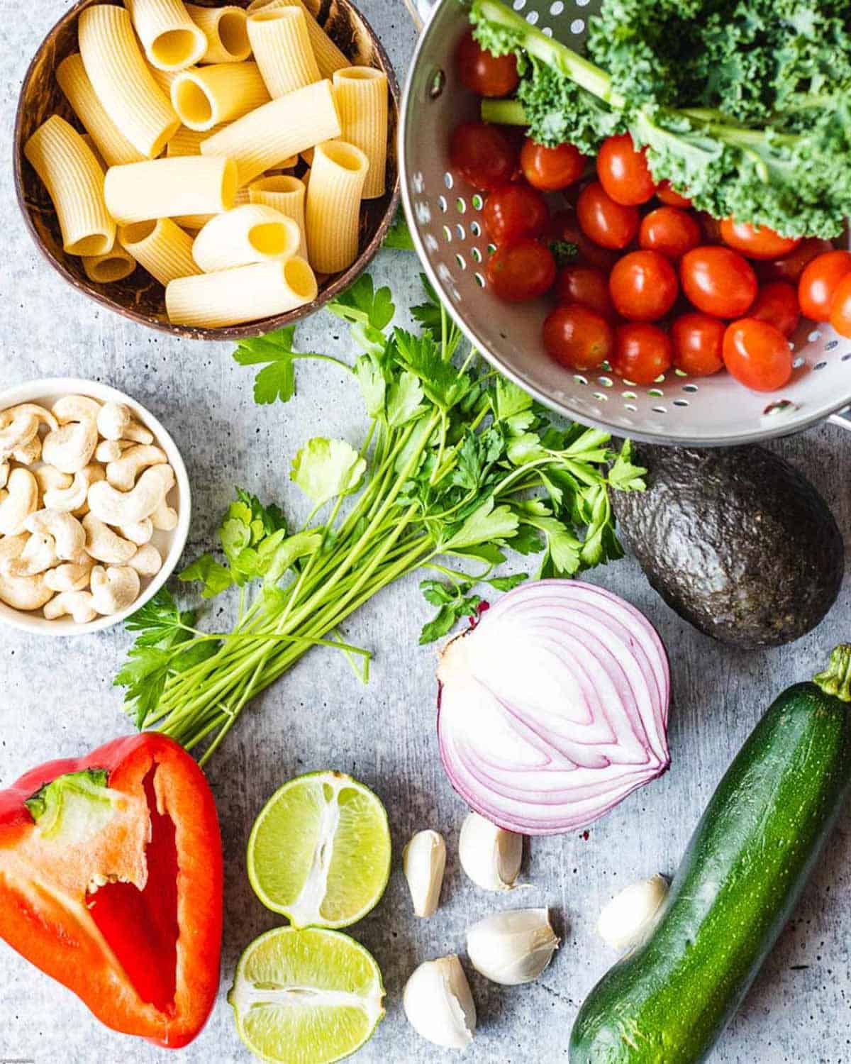 Ingredients for Roasted Vegetable Pasta Salad with Creamy Cilantro Dressing. Pasta, grape tomatoes, red bell pepper, zucchini, red onion, cashews, garlic, lime, and cilantro.