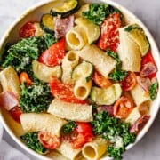 Rigatoni pasta with roasted curly kale, grape tomatoes, and red onion in a creamy light green cilantro dressing.