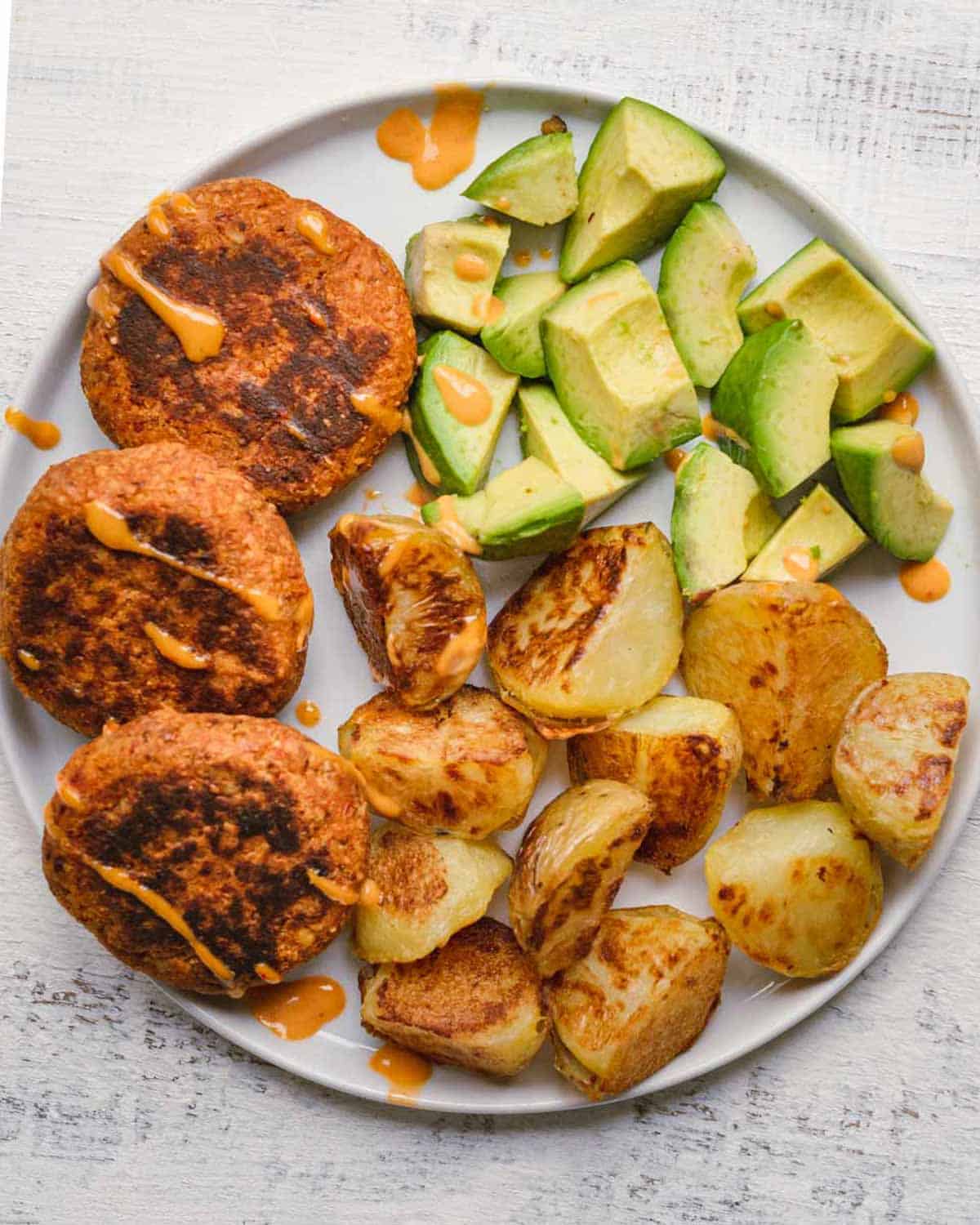 Sun-Dried Tomato Tempeh Burgers with crispy oven-baked potatoes and avocado chunks.
