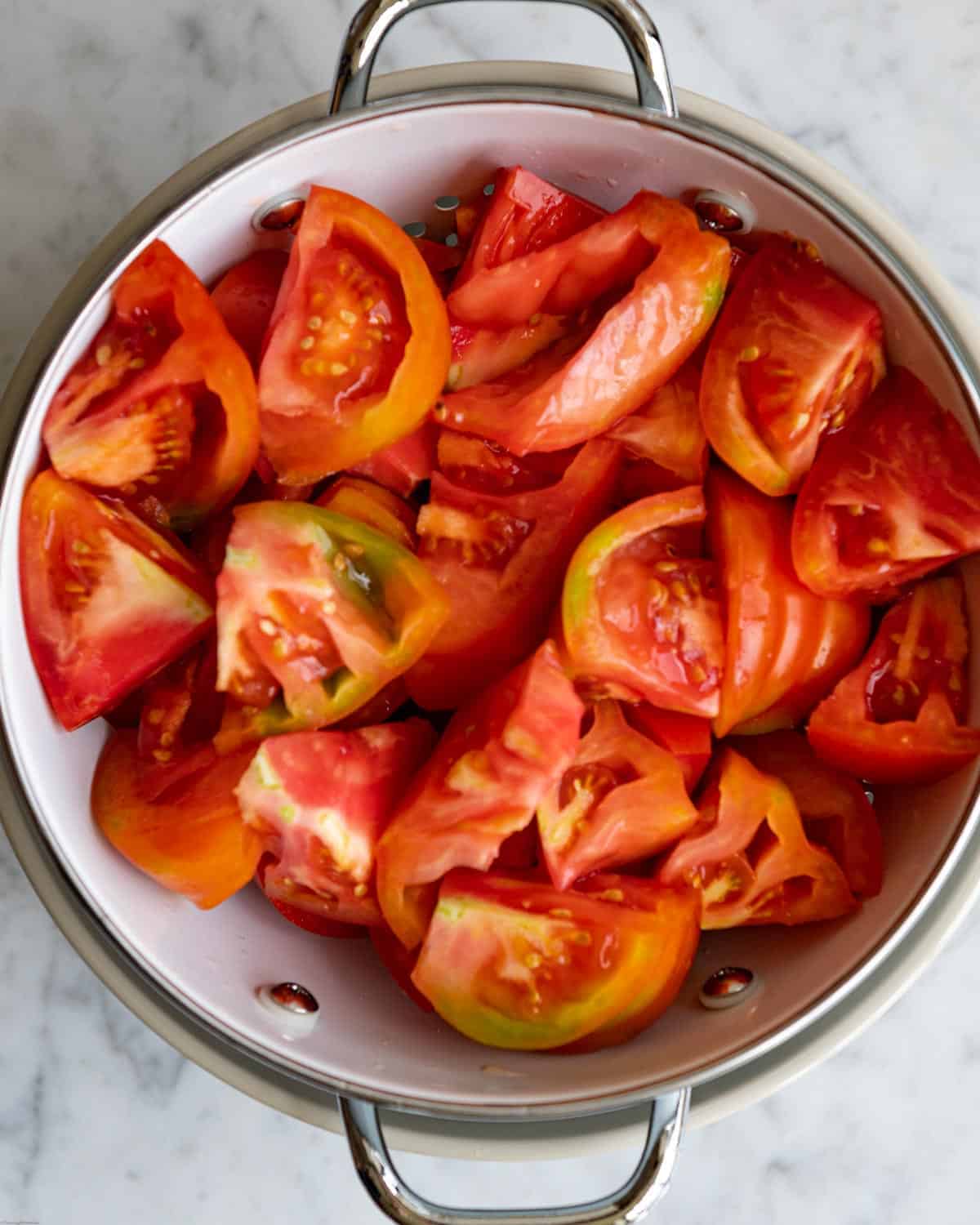 Heirloom tomatoes cut into bite-size pieces in a colander with kosher salt.