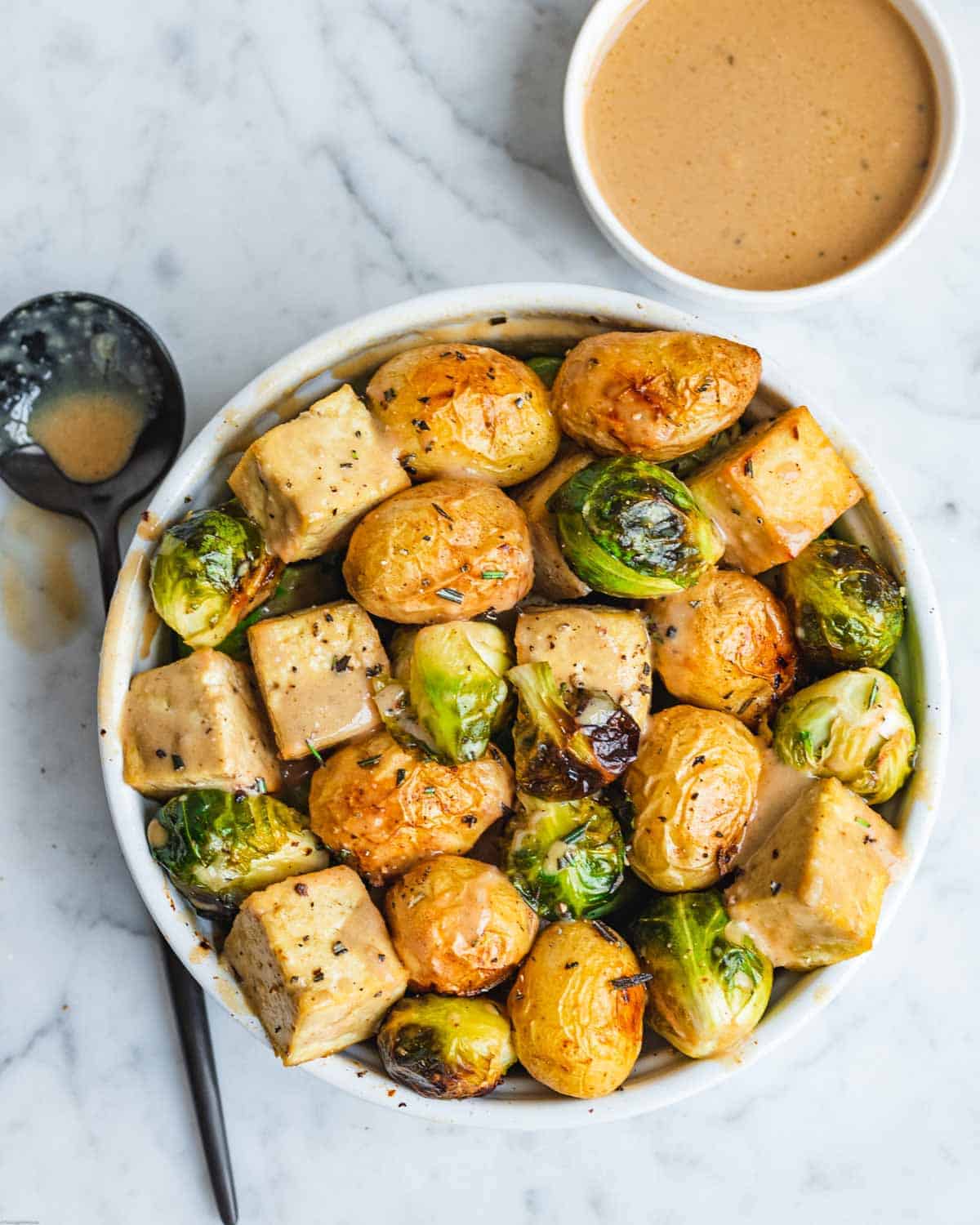 Roasted tofu, Brussels, and potatoes in a white bowl with Maple Dijon dressing.