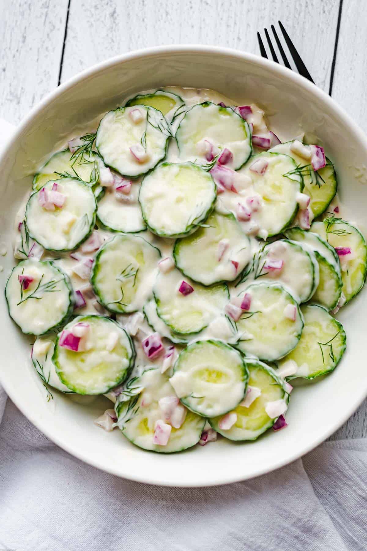 Easy creamy vegan dressing, cucumbers, chopped red onion, and fresh dill in a bowl ready for serving.