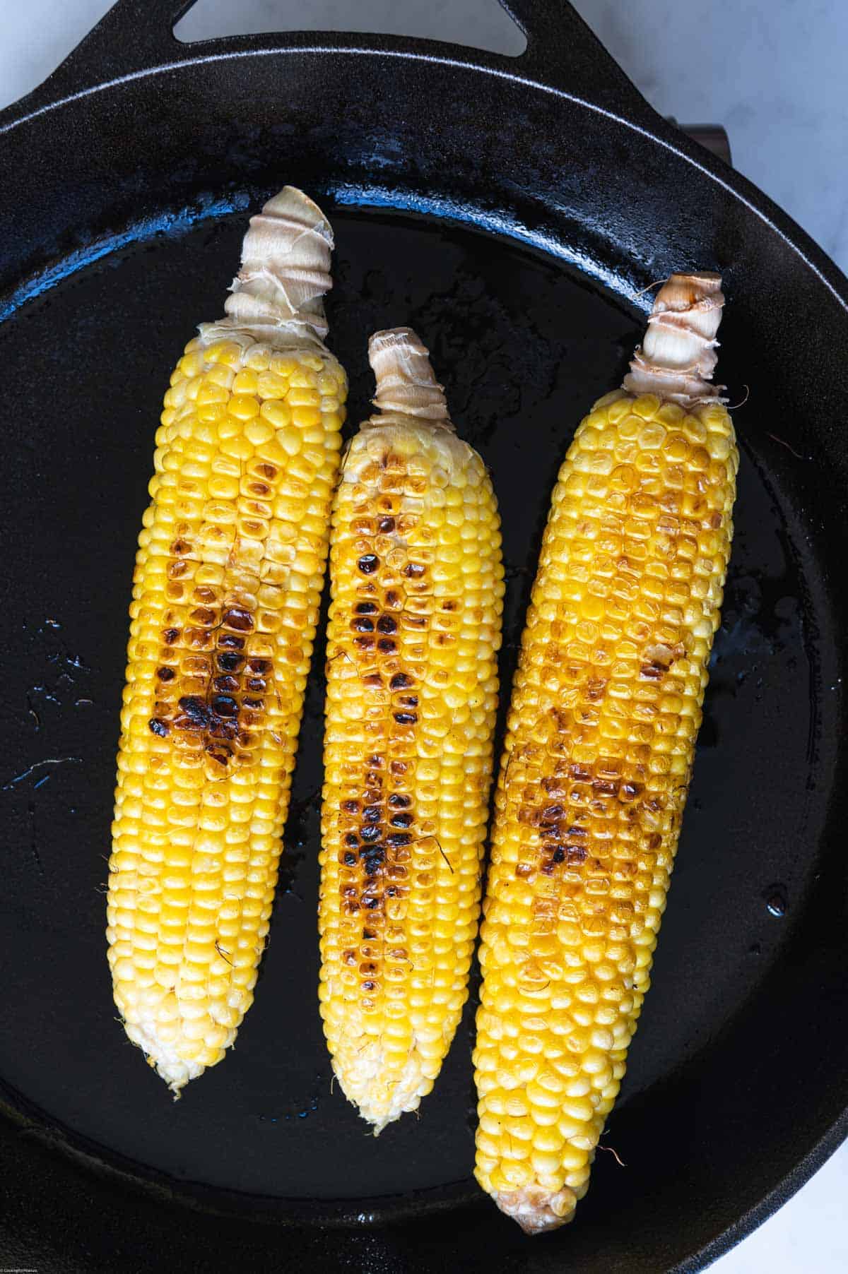 Three ears of charred corn in a skillet.