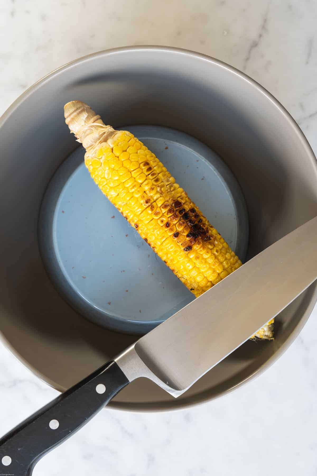 Chef's knife, small bowl inside a large bowl, one ear of corn.