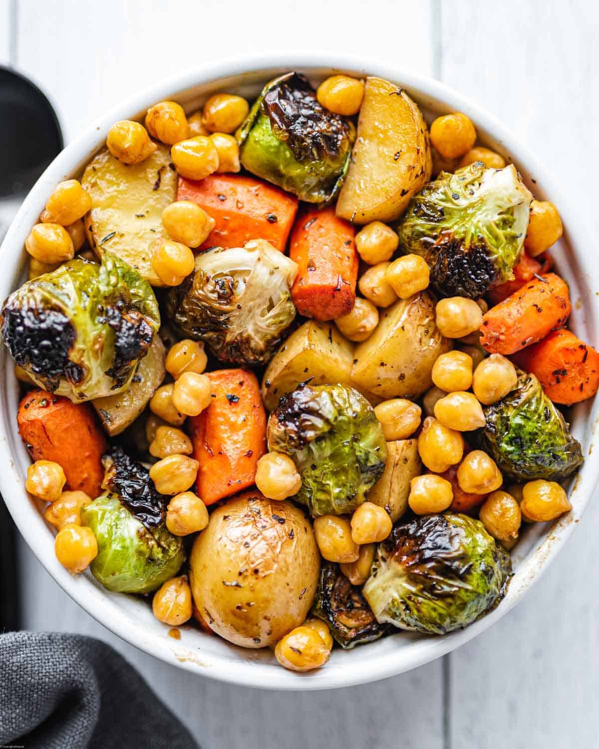 Roasted carrots, potatoes, Brussels sprouts, and chickpeas in a white bowl for serving.