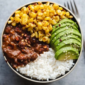Black bean chili, white rice, avocado, and sweet corn kernels in a bowl.