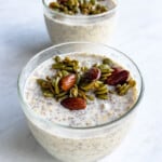 Overnight oats with chia seeds in two glass containers topped with pumpkin seeds, almonds, and sunflower seeds.