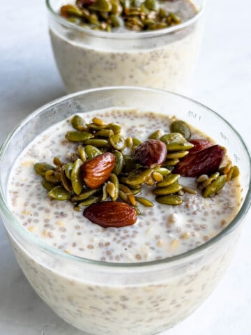 Overnight oats with chia seeds in two glass containers topped with pumpkin seeds, almonds, and sunflower seeds.