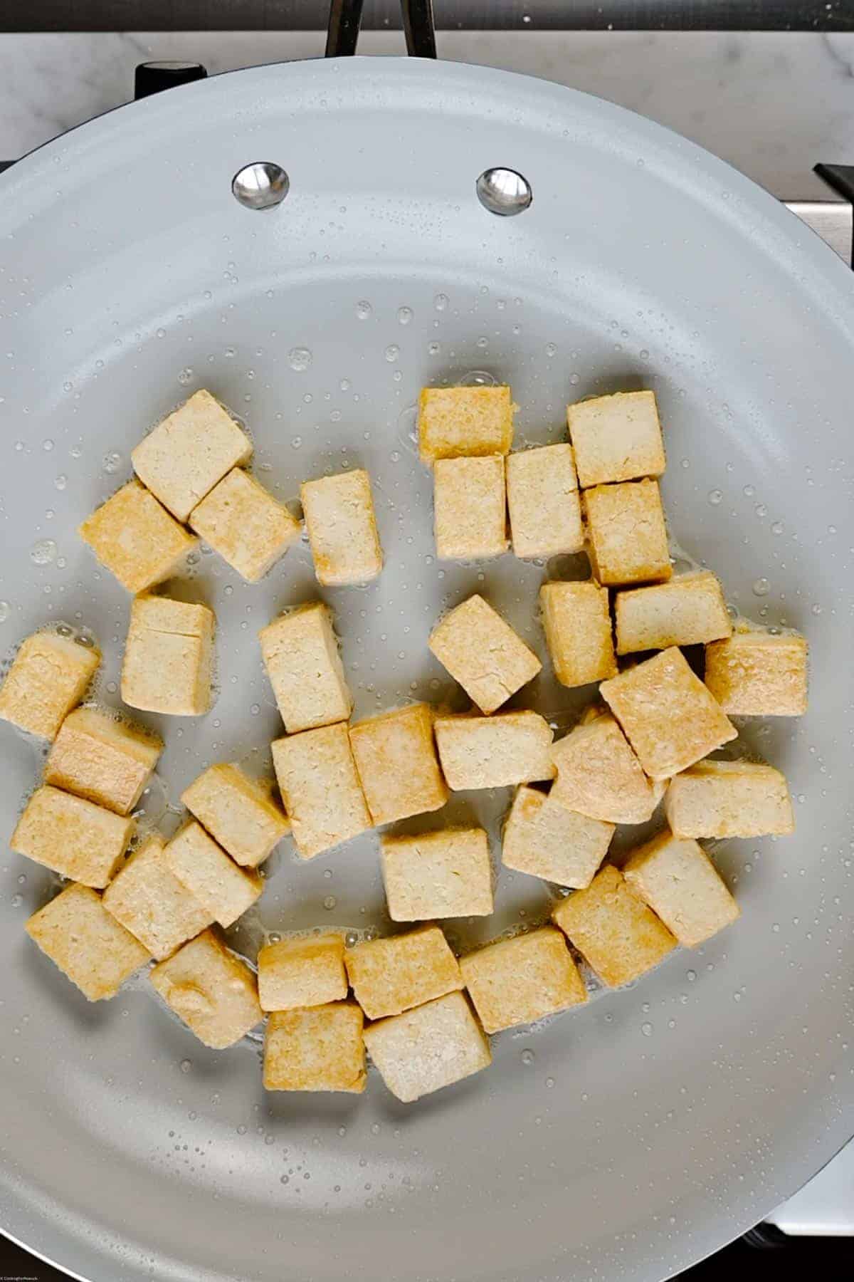 Tofu cubes pan-frying in a large nonstick skillet.