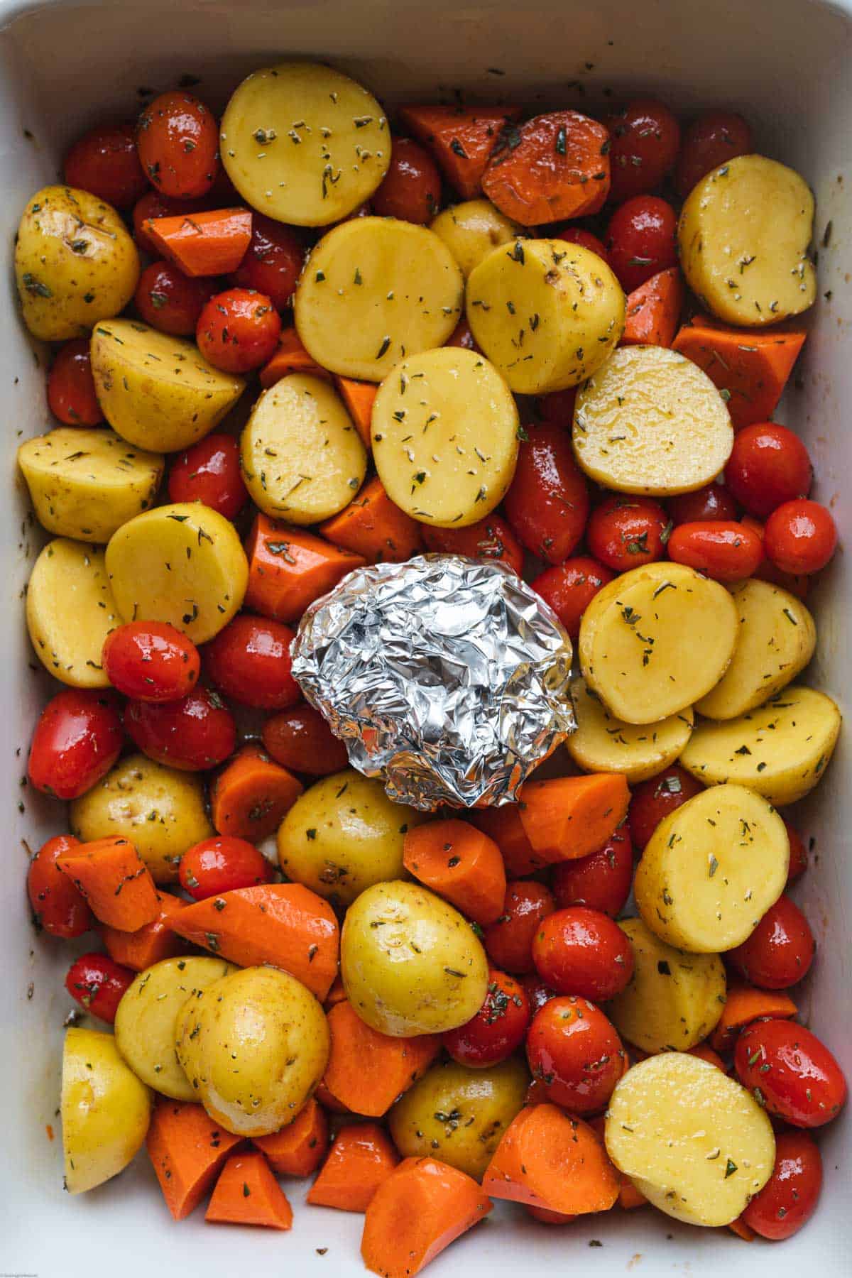 Baby potatoes, grape tomatoes, chopped carrots, and a head of garlic wrapped in aluminum foil in a large casserole dish. Tossed with herbs and olive oil.