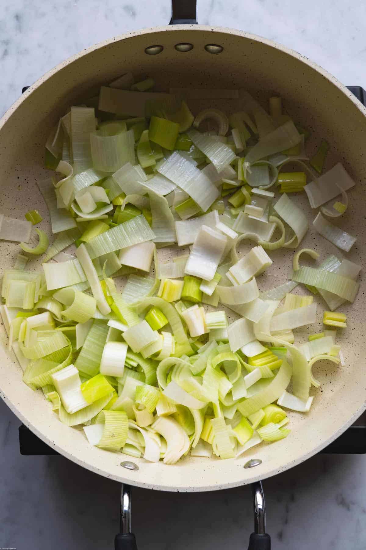 Softened sliced leeks cooking in olive oil in a large sauté pan.