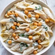 Creamy Vegan Artichoke Miso Pasta with crispy roasted chickpeas and spinach in a white bowl.