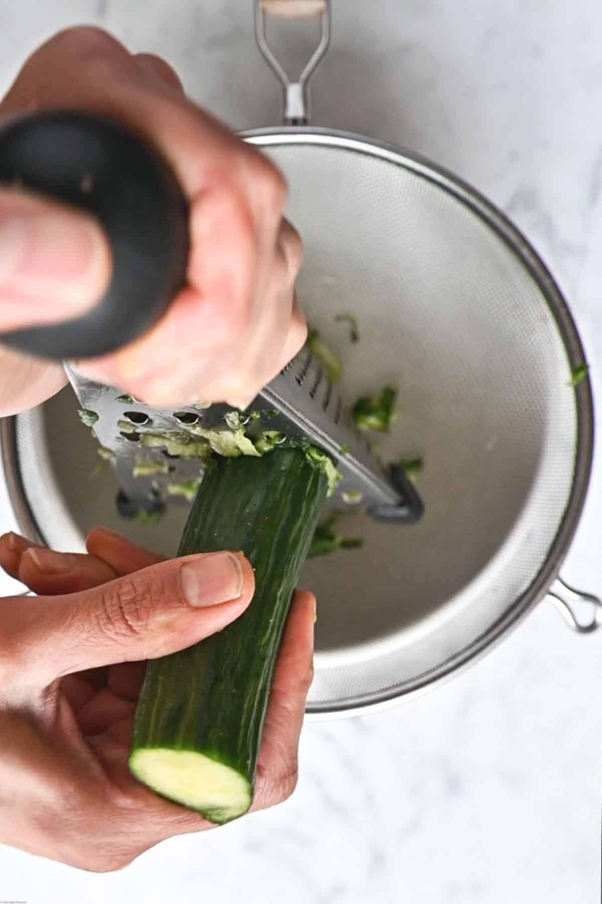 Cucumber being grated with the skin on using a box grater.