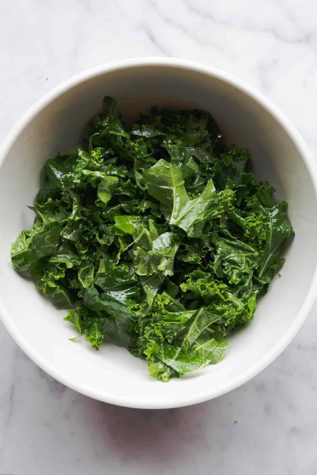Kale leaves with dressing in a white bowl.
