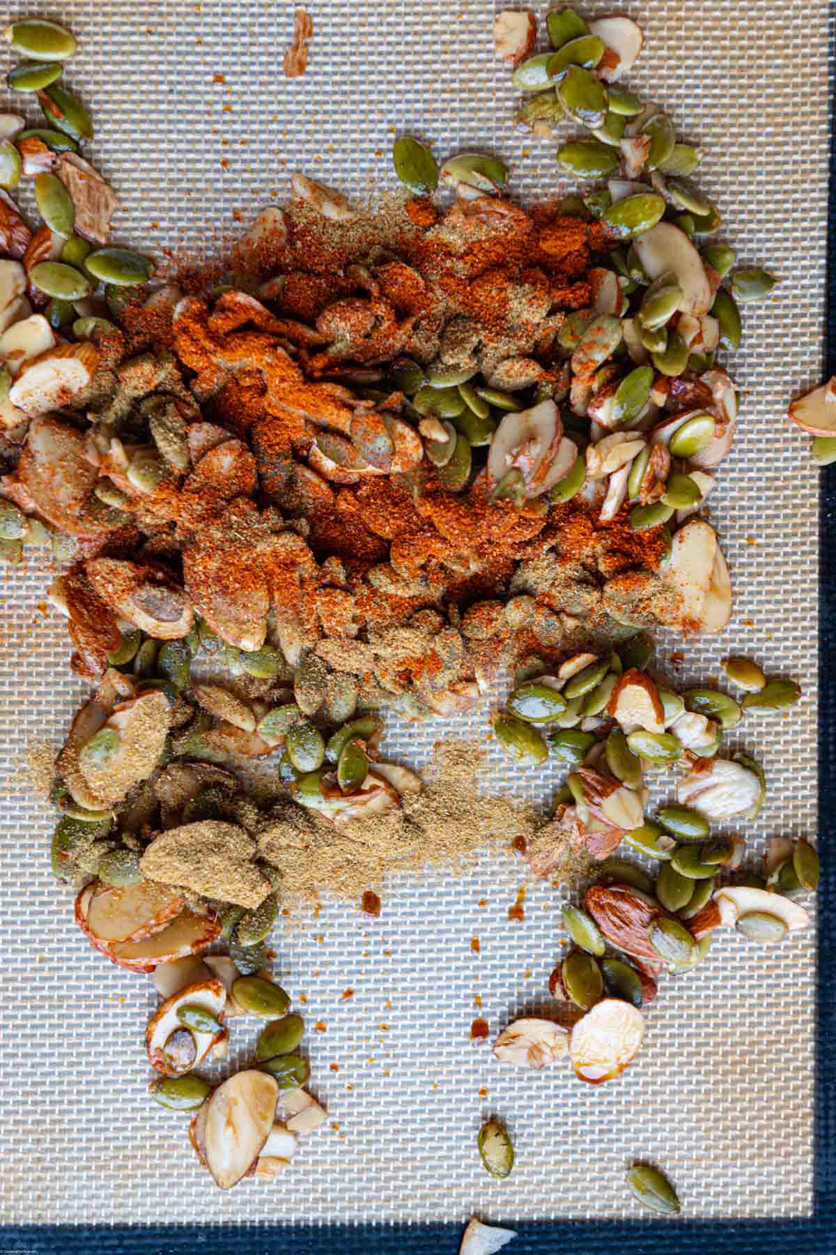 Slivered almonds and pepitas tossed with spices on a baking sheet.