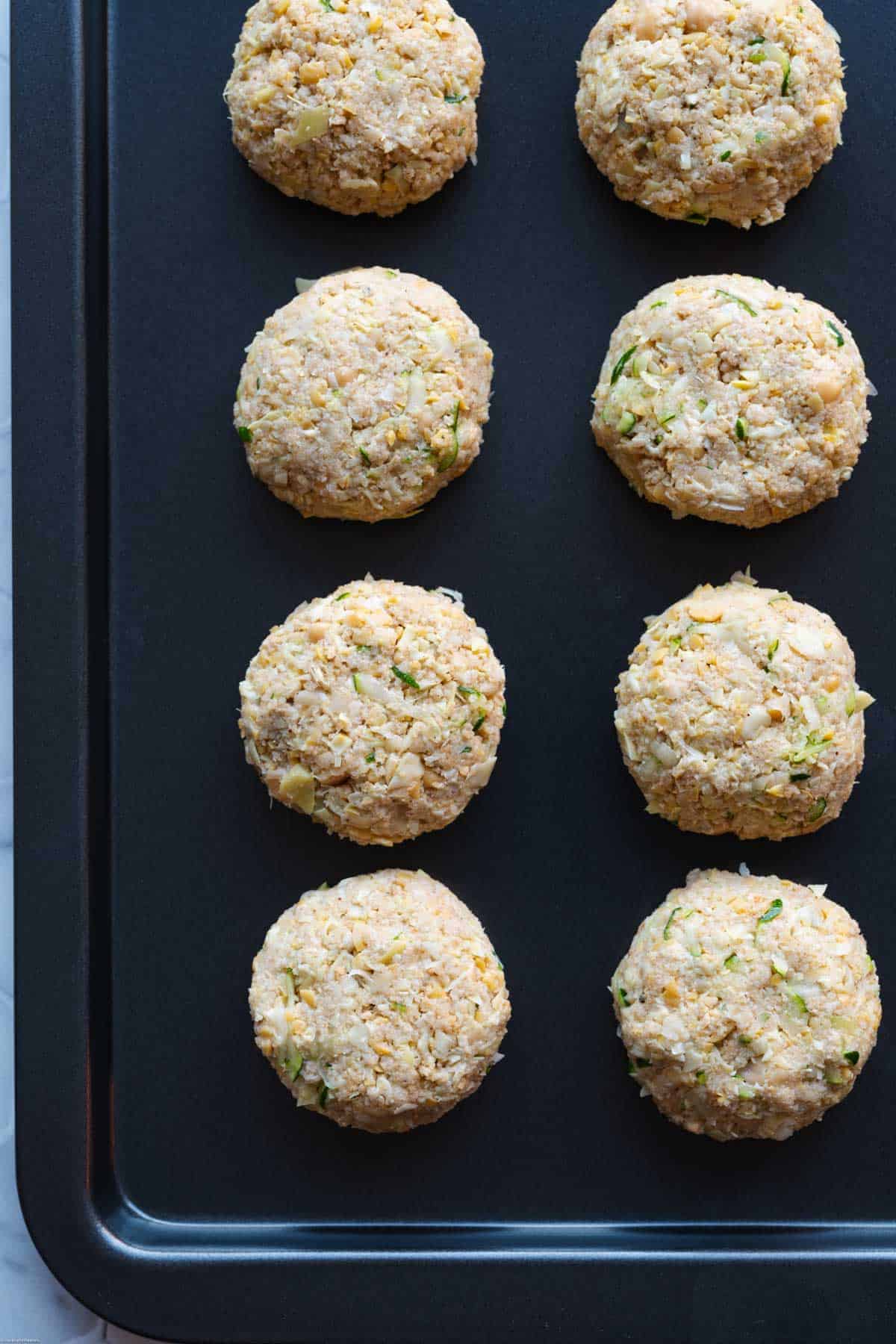 Eleven Vegan Crab Cakes with Artichoke Hearts on a large nonstick baking sheet ready to be baked.