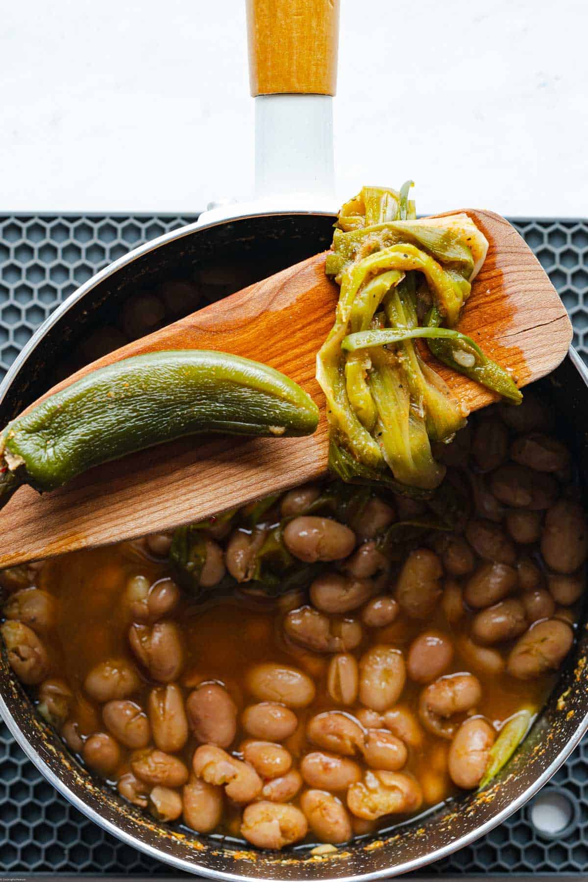 Green onions and jalapeño on a wooden spatula being removed from the saucepan of simmered beans.