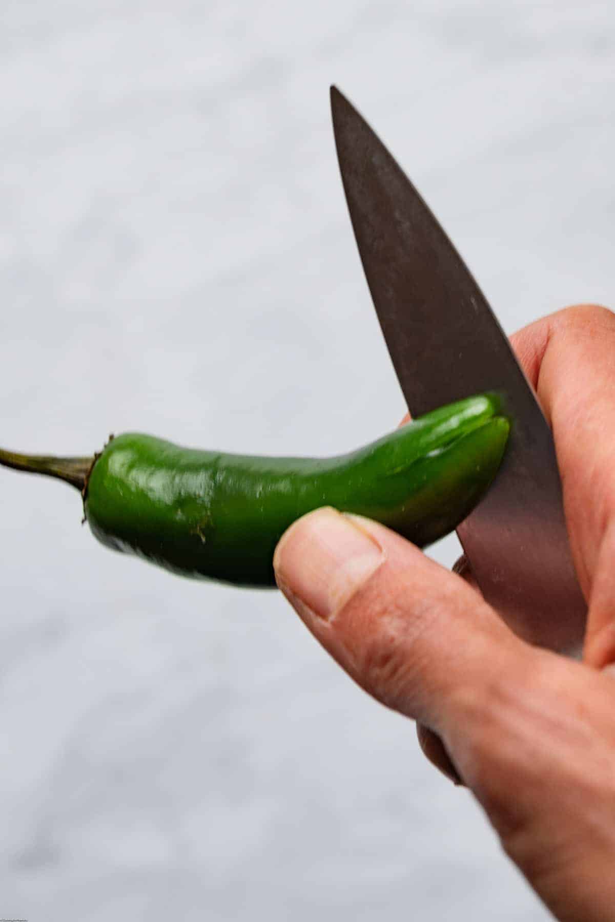 Scoring the bottom of the jalapeño with a small knife.