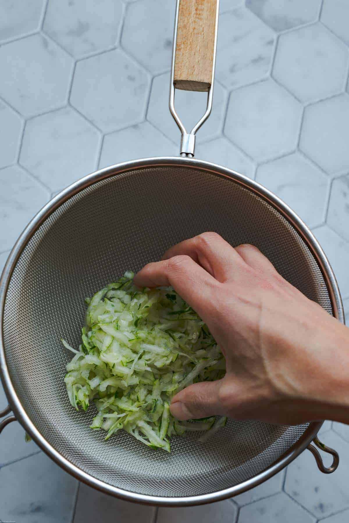 Grated zucchini in a large sieve over a bowl.