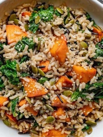 Kale & Sweet Potato Wild Rice Salad in a white bowl with a silver fork.
