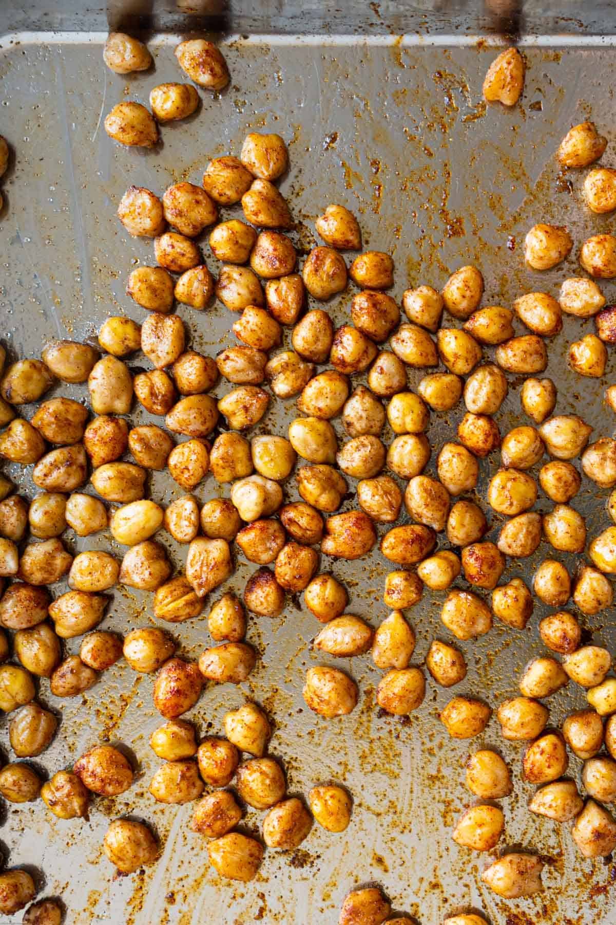 Crispy roasted chickpeas in five spice powder and olive oil on a stainless steel rimmed baking sheet.