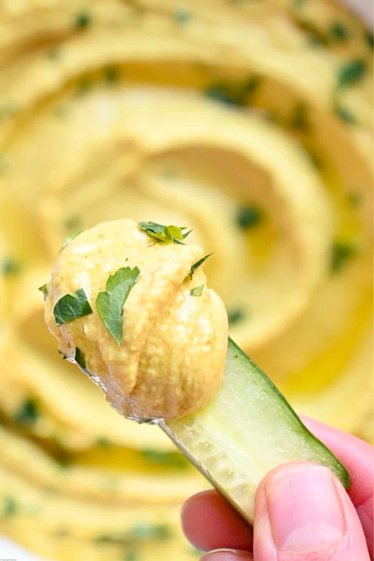 Bright yellow high-protein red lentil dip on a piece of cucumber held between fingers.