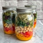 Ginger carrot dressing, shredded carrots, red bell pepper, chickpeas, kale, dried cranberries, pepitas and hemp seeds in 3 mason salad jars.