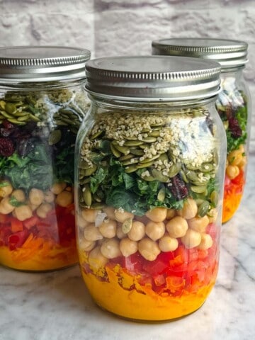 Ginger carrot dressing, shredded carrots, red bell pepper, chickpeas, kale, dried cranberries, pepitas and hemp seeds in 3 mason salad jars.