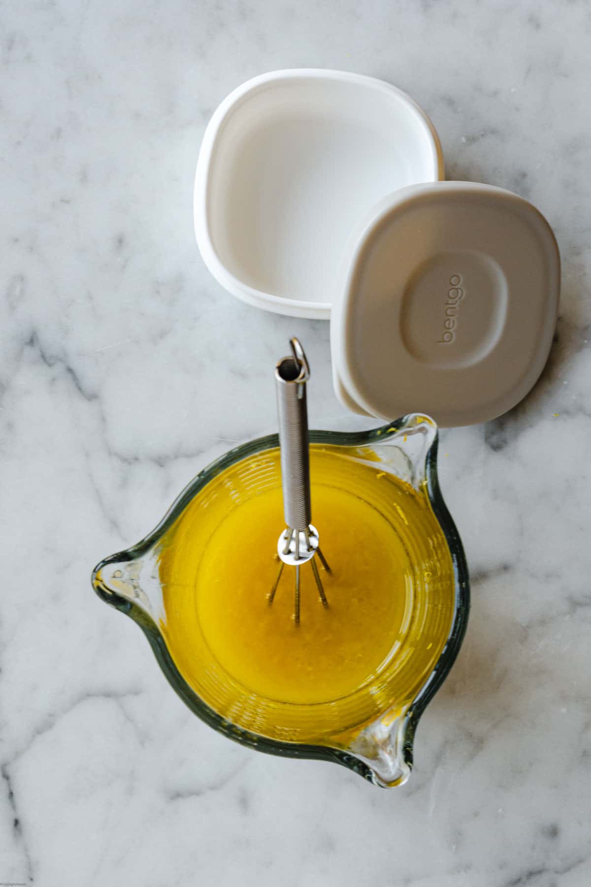 Lemony dressing in a glass measuring mug with a whisk next to a storage container.