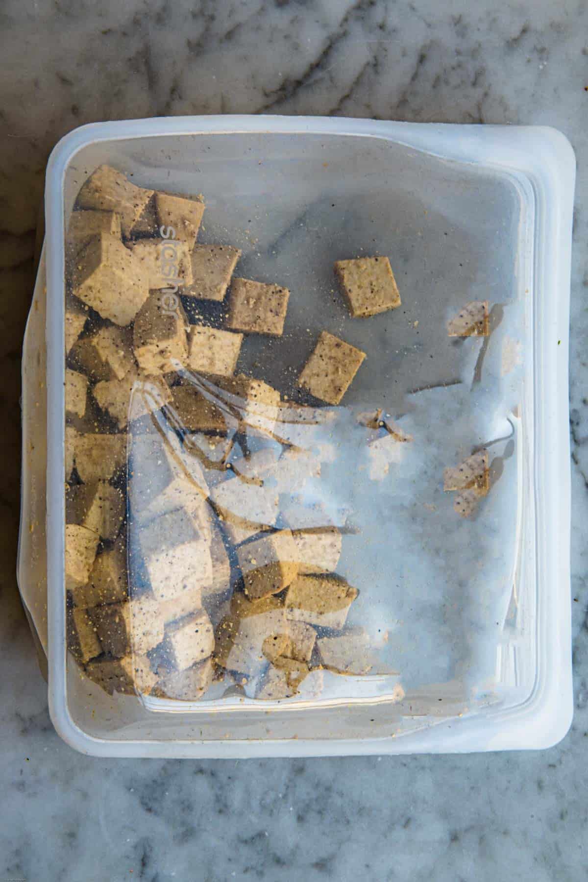 Tofu cubes with cornstarch, and seasoning in a reusable silicone bag for marinating.