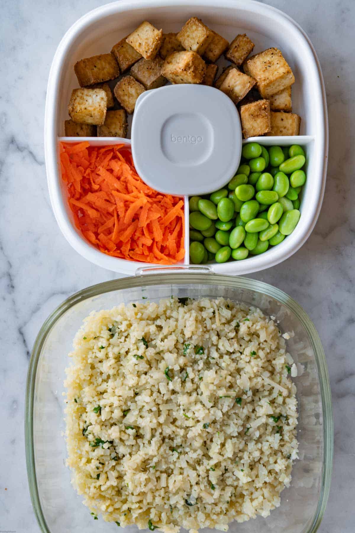 Cauliflower rice, air fryer tofu cubes, grated carrot, edamame, and peanut dressing in a bento lunch container.