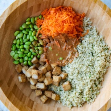 Cauliflower rice, air fryer tofu cubes, grated carrot, edamame, and peanut dressing in a wooden bowl.