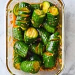 Mini cucumbers cut into accordions in a glass dish tossed with red Korean Gochugaru dressing.