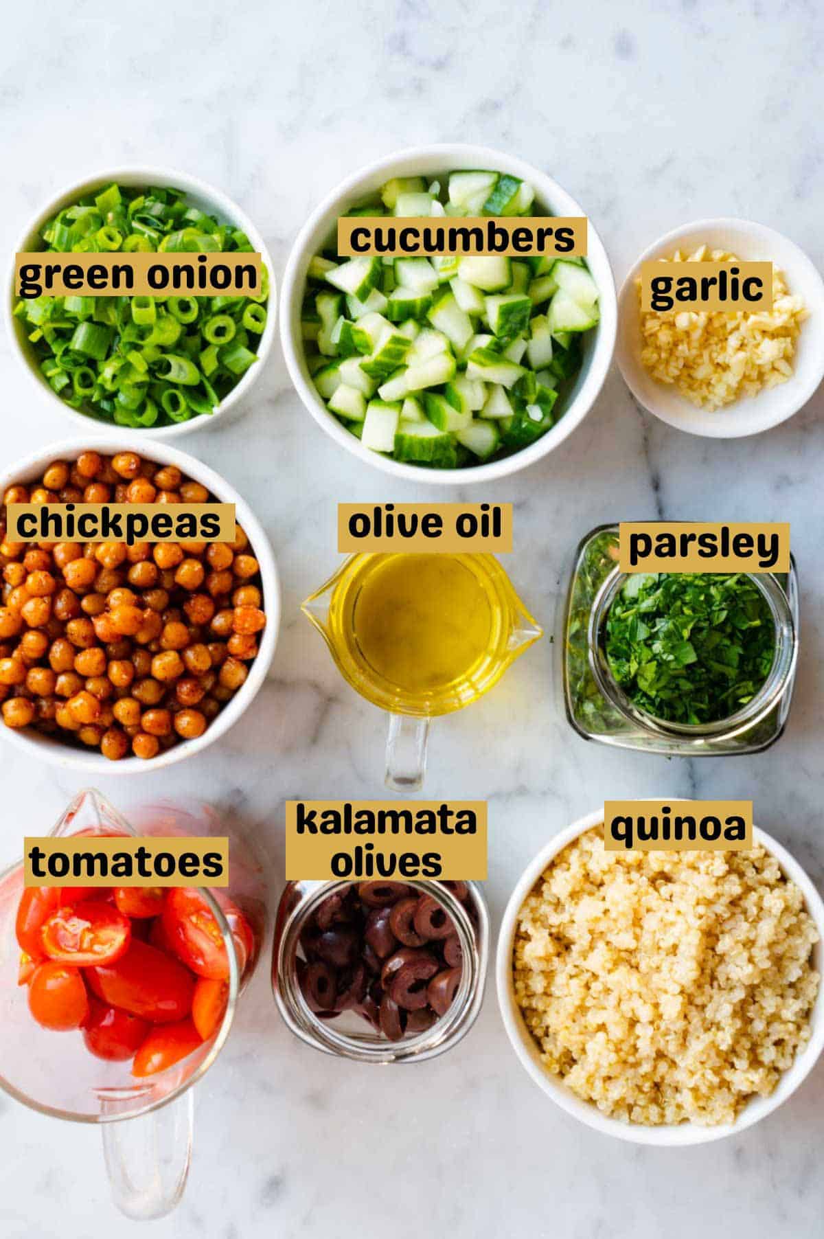Chopped green onion, cucumber, garlic, parsley, mint, grape tomatoes, and olives in jars with a bowl or quinoa, roasted chickpeas, and olive oil.