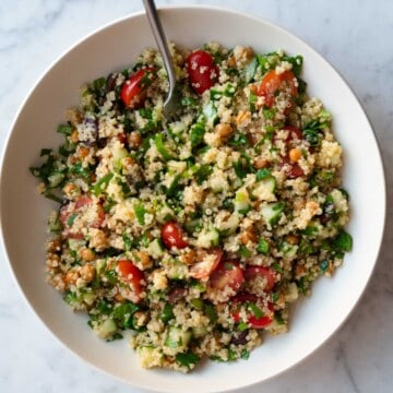 Gluten-free quinoa tabbouleh salad with grape tomatoes, chopped parsley, mint, and green onion, olives, and roasted chickpeas in a white bowl.