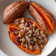 Sliced orange sweet potato stuffed with roasted chickpeas, red cabbage, dried cranberries, pecans, pepitas, and creamy dressing on a plate with two more air fryer sweet potatoes.