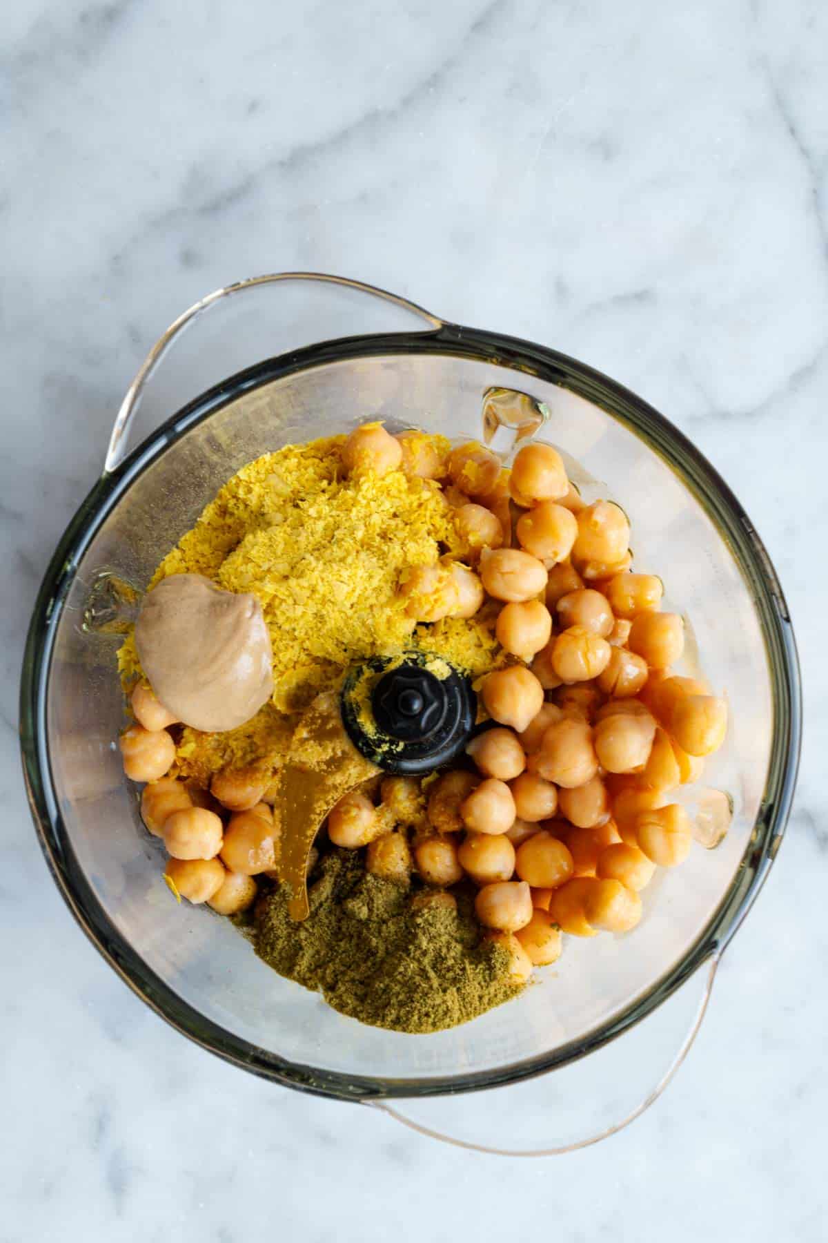 Nutritional yeast, chickpeas, Dijon, and seasonings in the canister of a food processor.