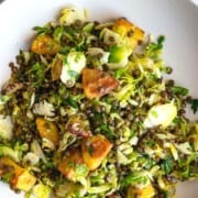 Warm shaved Brussels sprout salad, roasted lentils, potato croutons, chopped pecans, and parsley in dressing, mixed and plated.