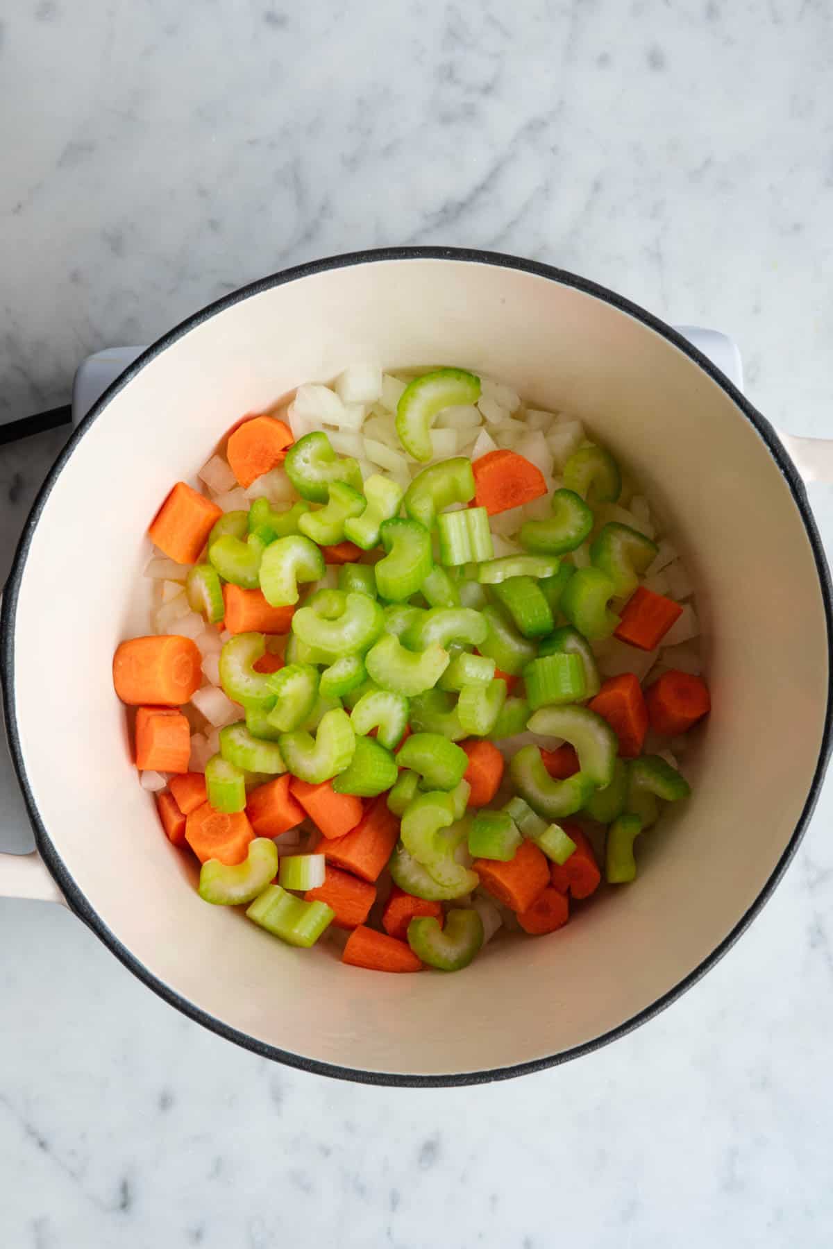 Chopped onion, carrots and celery cooking in a white saucepan.