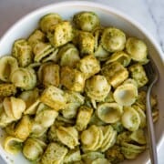 Green pesto with baked tofu and orecchiette pasta in a white bowl with a silver fork.
