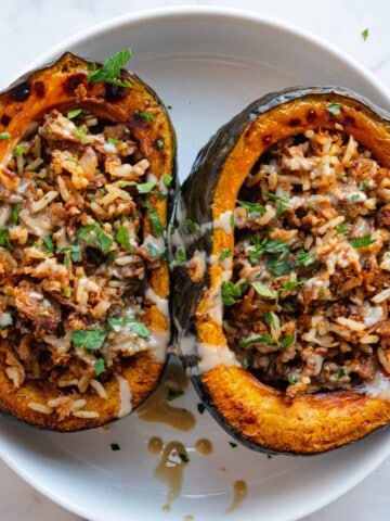 Roasted kabocha squash halves, stuffed with tofu taco meat and rice, and topped with a drizzle of tahini and chopped parsley.
