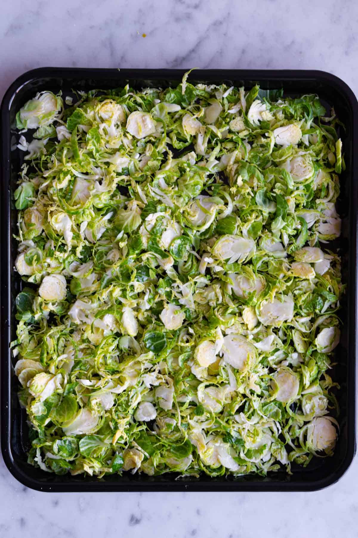 Shaved Brussels sprouts on a black nonstick rimmed baking sheet.