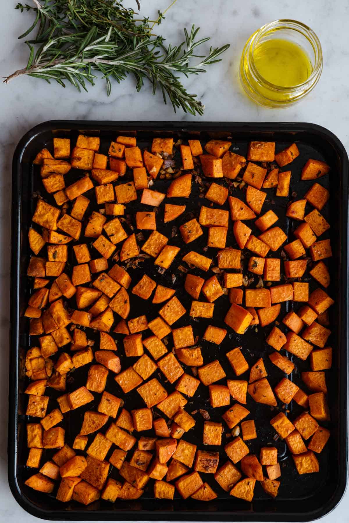 Roasted sweet potato cubes on a black baking tray.