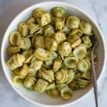 Orecchiette pesto pasta and baked tofu in green pesto in a white bowl with a silver fork.