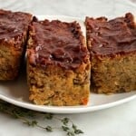 Three mini vegan meatloaf on a white plate with fresh thyme leaves.