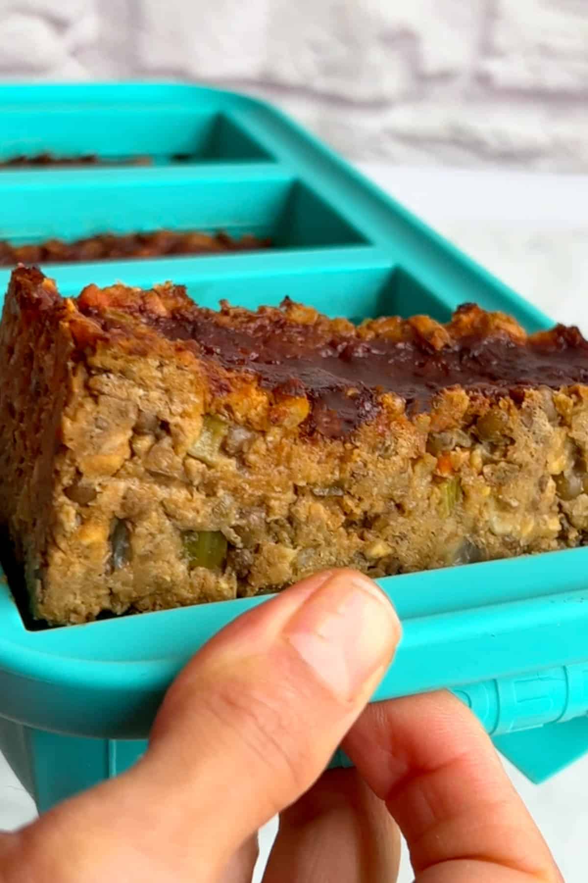 Vegan meatloaf popping out from a one cup sized turquoise soupercube freezer tray.