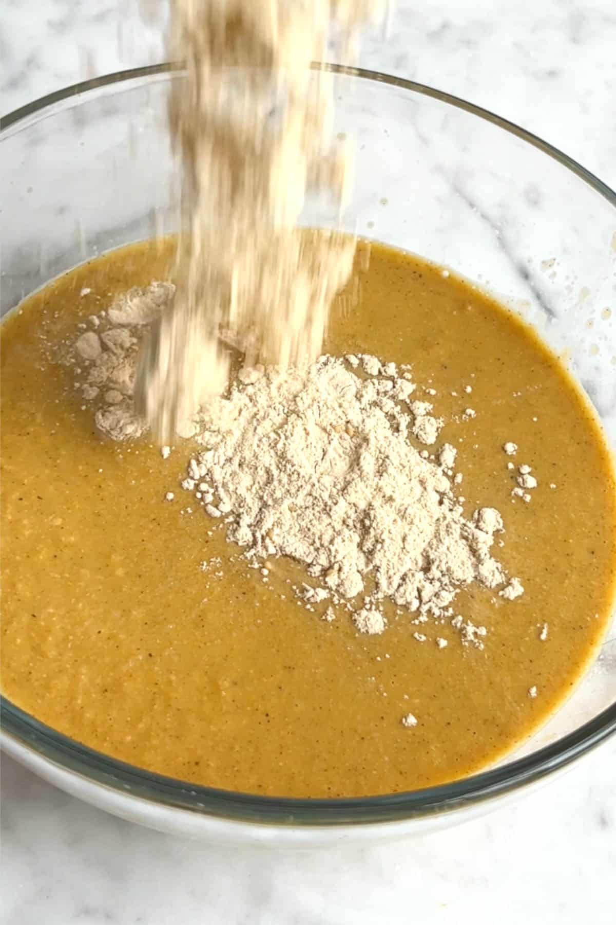 Blended mustard colored liquid with white flour dusted in top in a glass bowl.