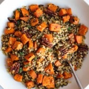 Warm quinoa salad with tricolor quinoa, roasted sweet potato cubes, chopped pecans, and fresh thyme leaves in a white bowl with a fork.
