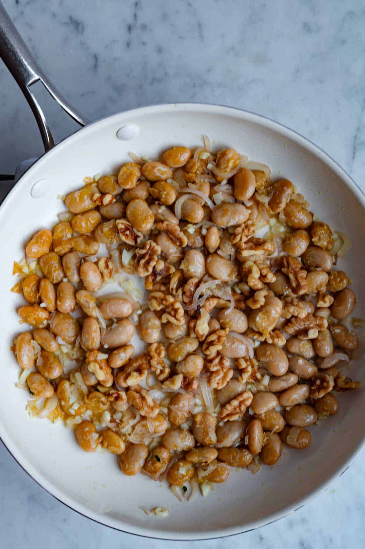 Crispy butter beans with walnuts, shallot, and garlic in a white skillet.